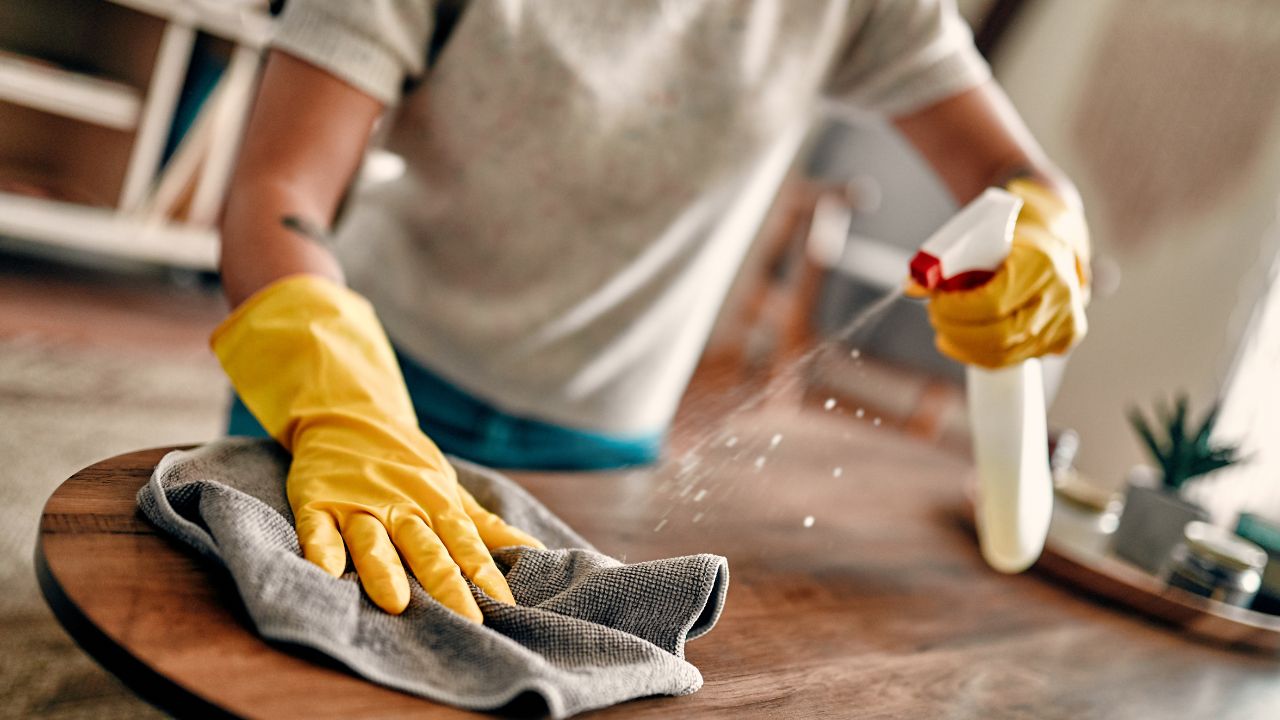 Person wearing yellow gloves spraying and wiping down a wooden countertop